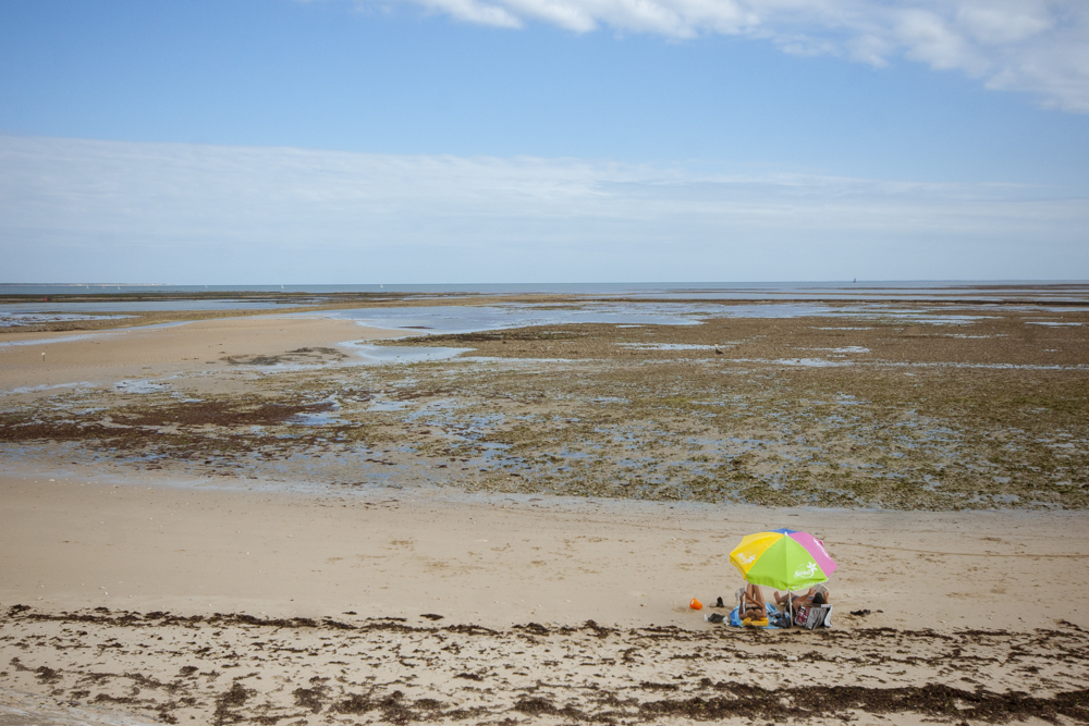 Sur une plage complétement désertique de l'Ile de Ré, un couple est installé sous son parasol.