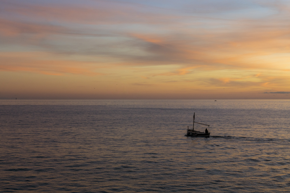 Un petit bateau de pêche partant vers le large au soleil couchant depuis le port de Cassis.