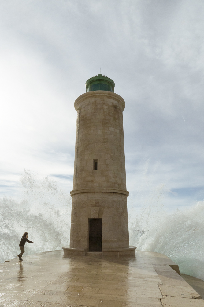 Un jeune garçon tente d'éviter de se faire arroser par une déferlante qui se brise sur la digue du port de Cassis.