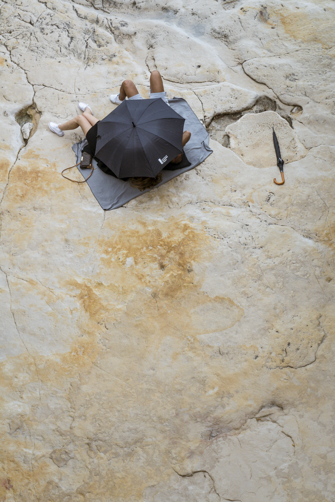 Un couple d'amoureux allongé sur les rochers se cache derrière son parapluie.