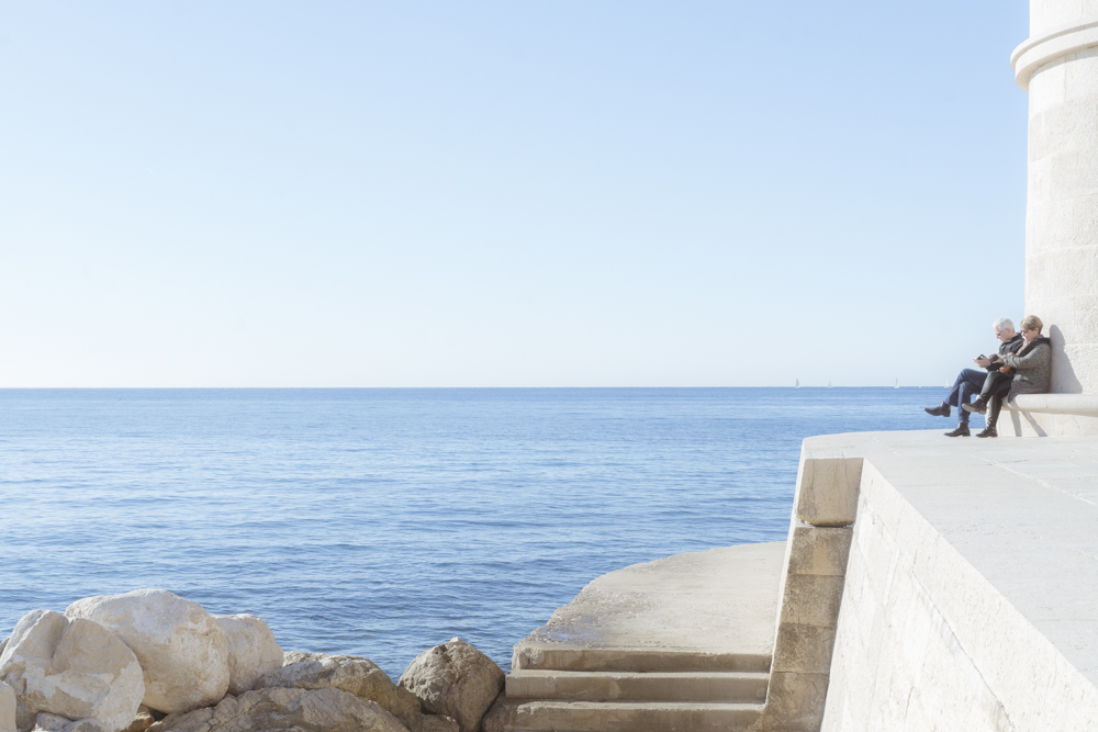 Un couple de sénior assis au phare de Cassis perdu dans la lecture de leur portable avec pourtant la Méditerranée qui s'offre à eux. 