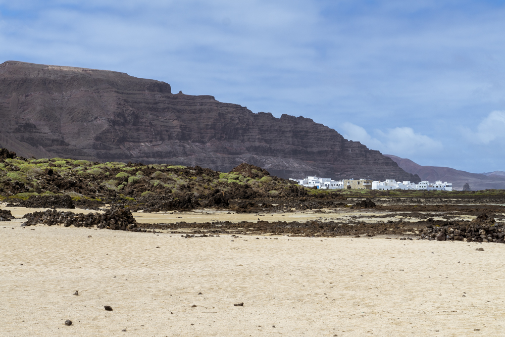 Un village aux maisons blanches calé entre un montagne noire et des plages de sables blancs.