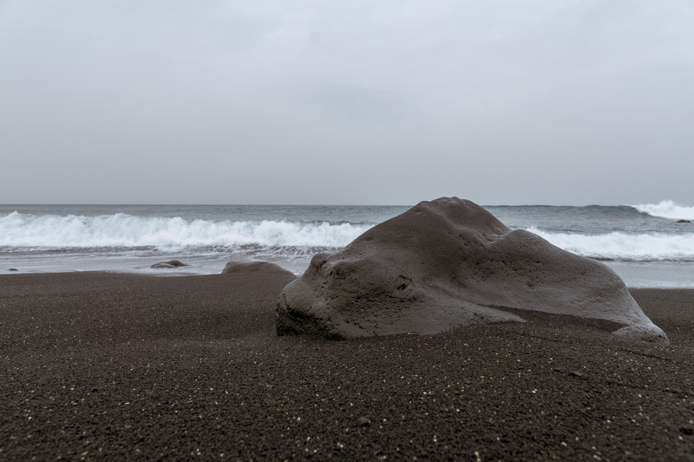 Une pierre ressemblant à une sorte de gros poisson sur une plage de sable noir.