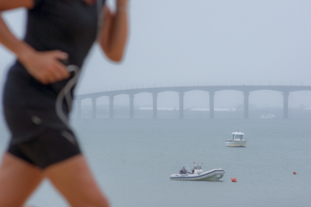 Une ou un joggeur court le long de l'Océan Atlantique avec le pont de l'Ile de Ré en arrière-plan.