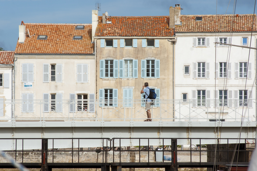 Un homme, appareil photo autour du coup observe ce qui pourrait faire une photo sur une écluse de Saint-Martin-de-Ré.