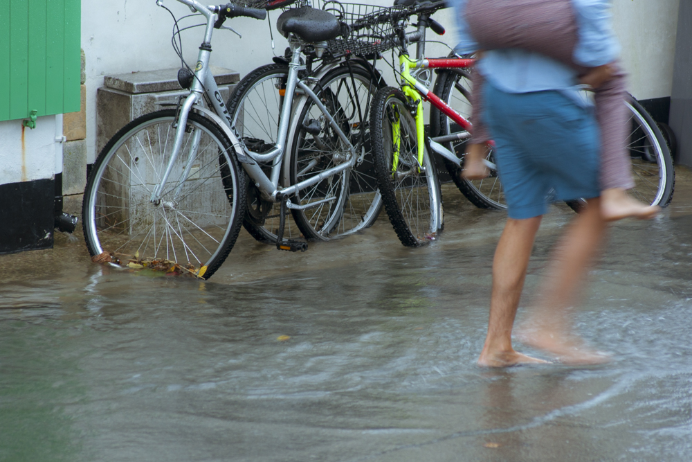 Un homme, portant sur son dos un enfant, marche pieds nus dans la rue envahie par les eaux.