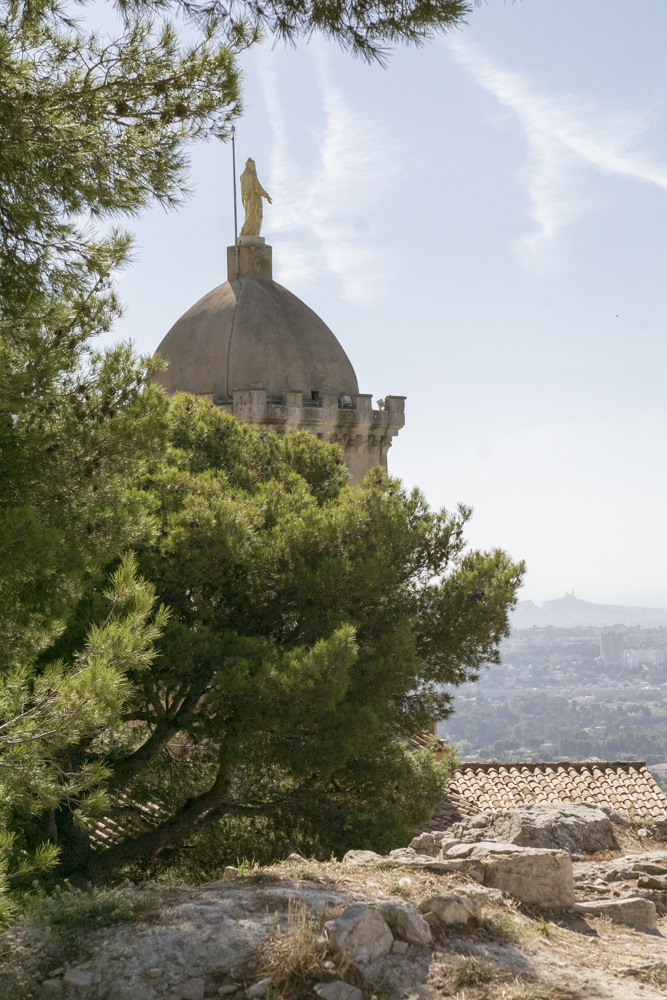Le clocher de la chapelle Notre-Dame du Château orné d'une statue en or de la Vierge, surplombe tout Marseille avec Notre-Dame de la Garde en arrière-plan.