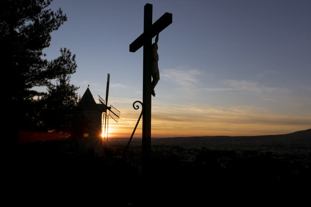 Le Christ sur sa croix au pied des moulins du village d'Allauch sous le soleil couchant.