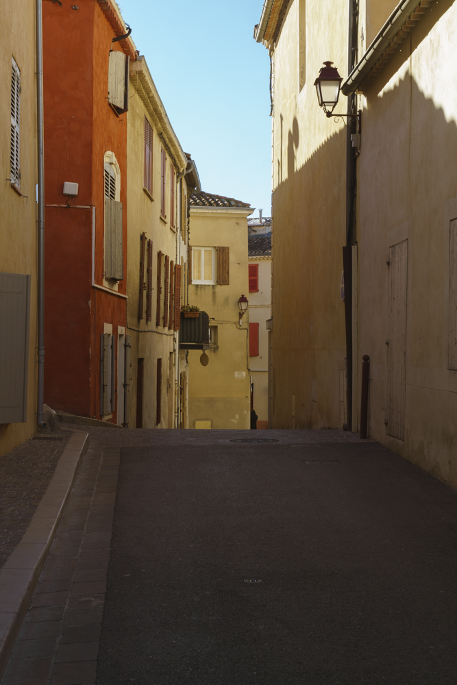 Des façades de maison de village de couleur jaune, ocre, sous un ciel bleu.