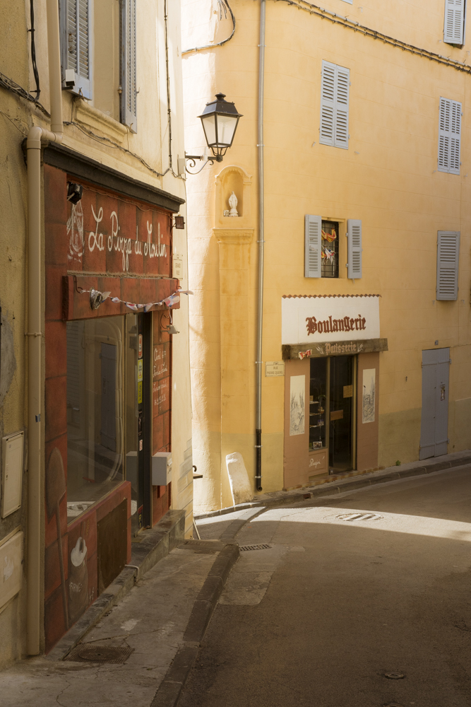 Une rue ombragée du village d'Allauch éclairée par un trait de lumière.