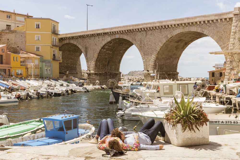 Un couple damoureux allongé sur un quai du port des Vallon des Auffes profite de la douceur du soleil de mai pour se relaxer.