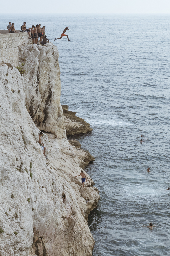 Un groupe dadolescents sur les hauteurs de la Corniche Kennedy à Marseille sélancent tour à tour pour sauter dans la Méditerranée une dizaine de mètre plus bas.