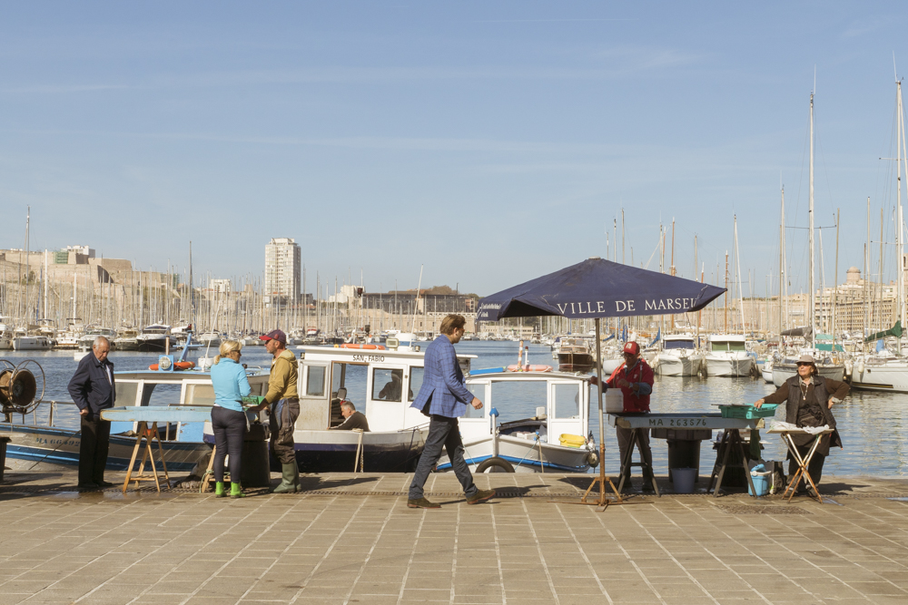 Un homme en costume se dirige vers un étal de poisson sur le Vieux-Port à Marseille.