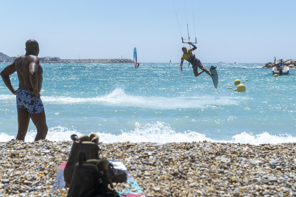 Un kitesurfeur réalise ses figures acrobatiques devant le regard attentif d'un homme en maillot de bain.