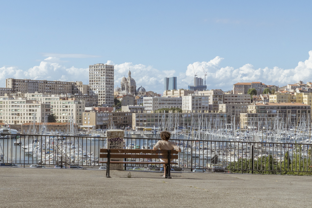 Une femme assise sur un banc contemple les vieux-port de Marseille.