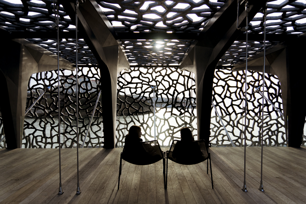 Deux jeunes filles installées dans des fauteuils que lon trouve sur le toit-terrasse du MuCEM, sont en pleine discussion avec pour horizon le soleil couchant filtré par la dentelle du MuCEM. 