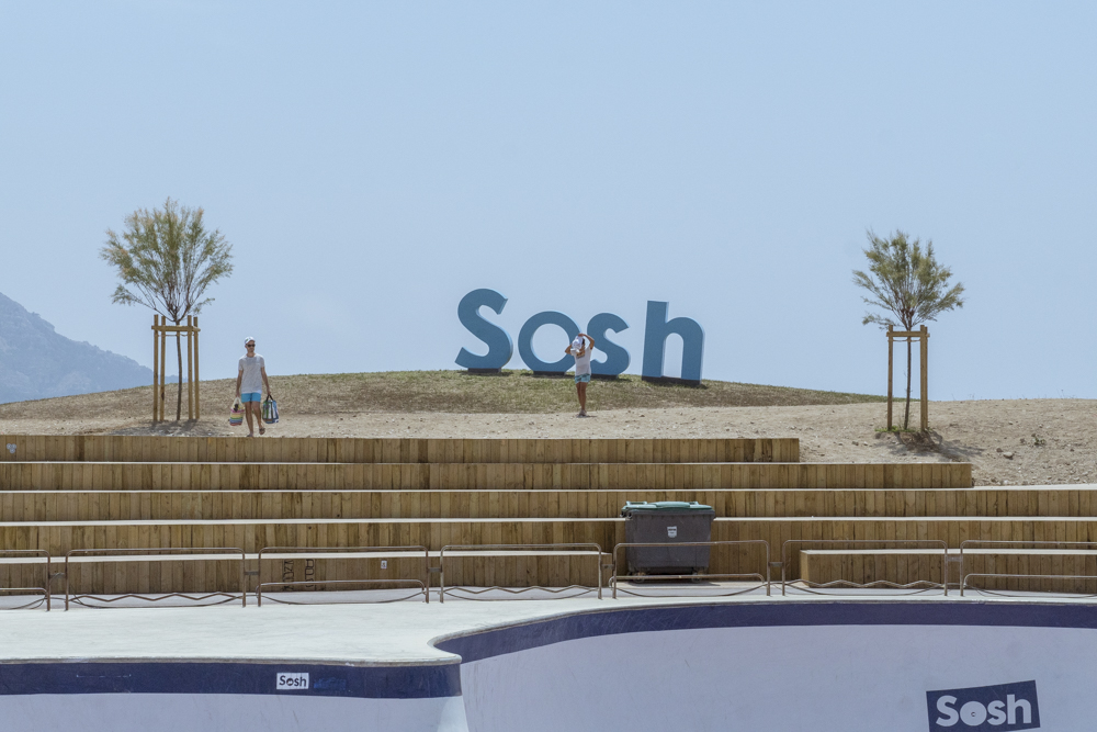 Un père avec sa fille, à la traine derrière lui, passe devant un logo Sosh a proximité du Skate Park du Prado.