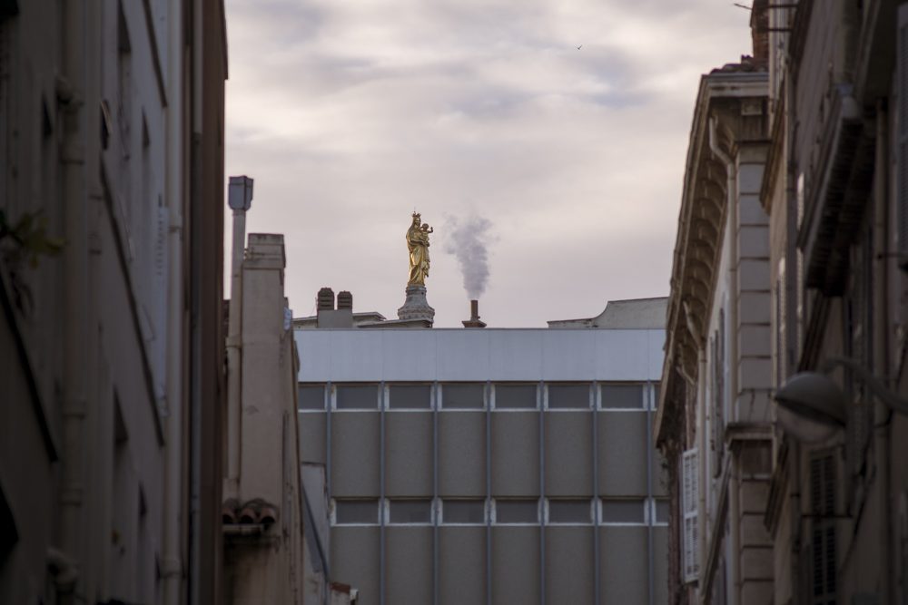 Depuis la rue du Petit Chantier dans le 7ème arrondissement de Marseille, par-dessus les toits dépasse juste la statue en or qui orne Notre Dame de la Garde.