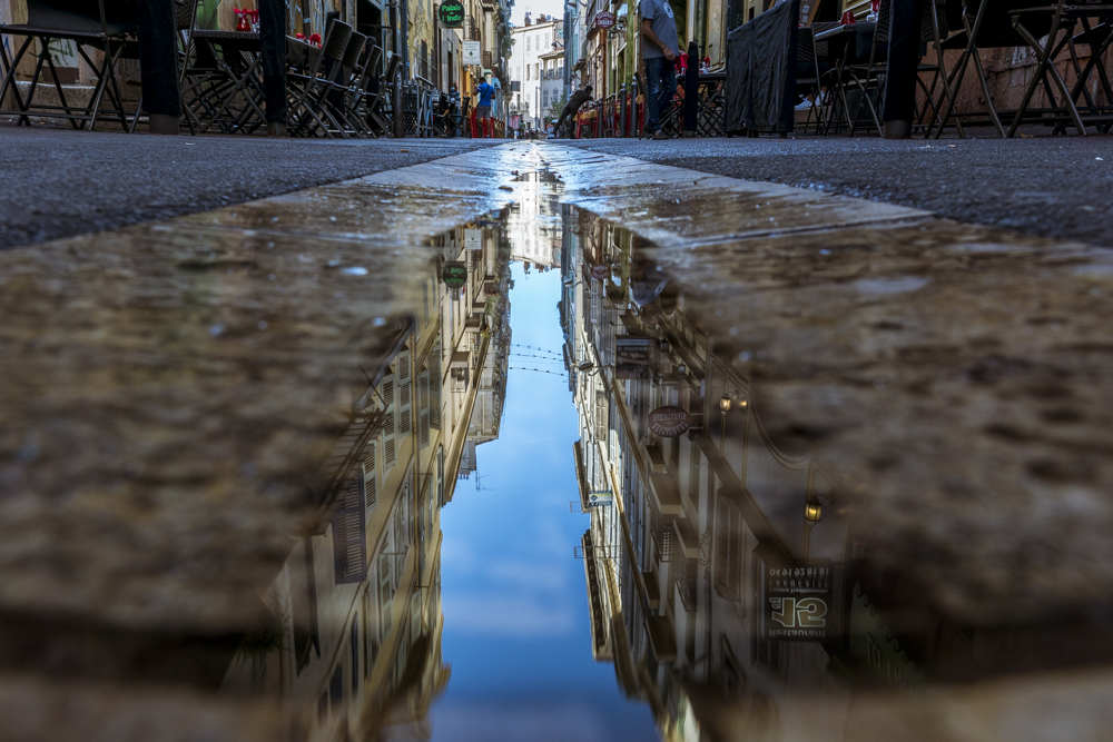 Au milieu de la rue des Trois Rois au Cours Julien, le ciel bleu se reflète dans le caniveau 