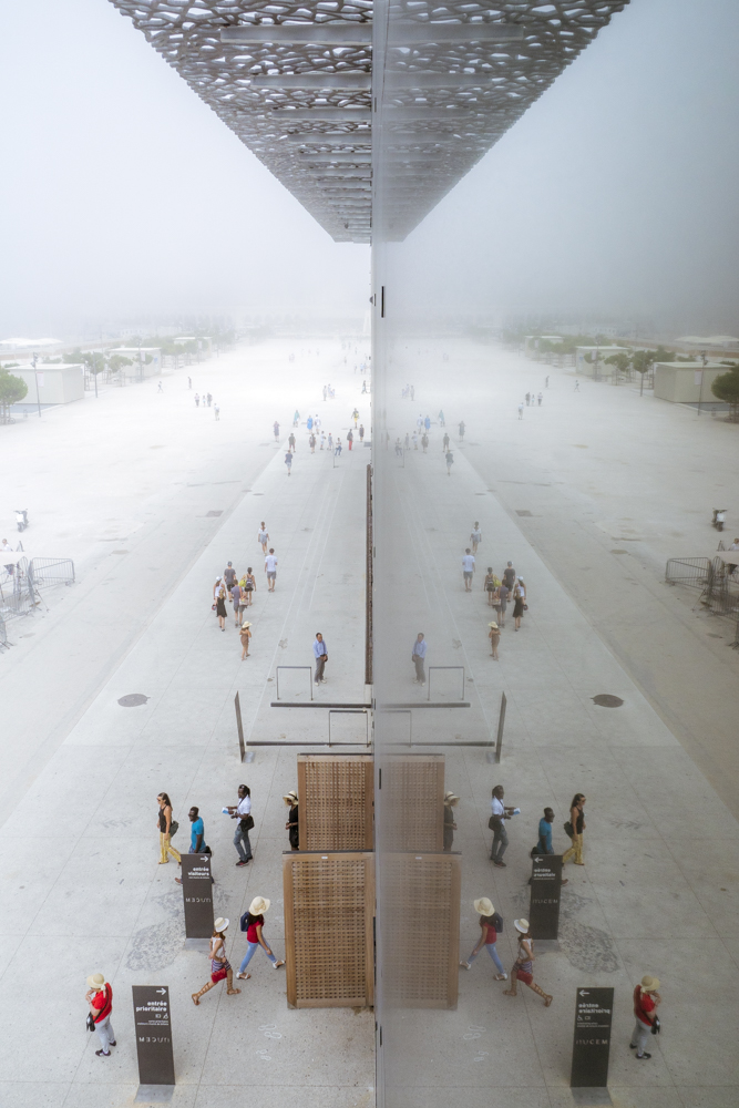Le reflet de la foule dans la façade du MuCEM, le tout dans une atmosphère brumeuse.